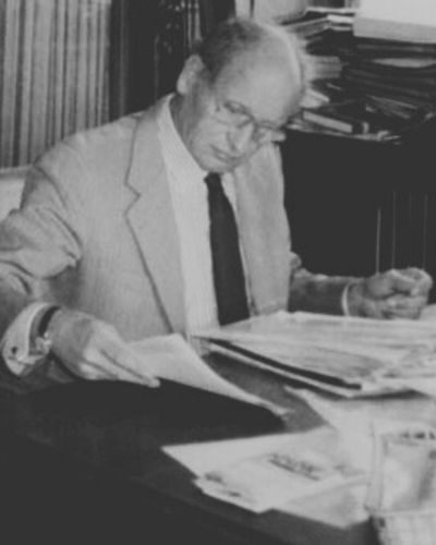 Dr. Rolf M. Schwiete (an seinem Schreibtisch beim Zeitungslesen)